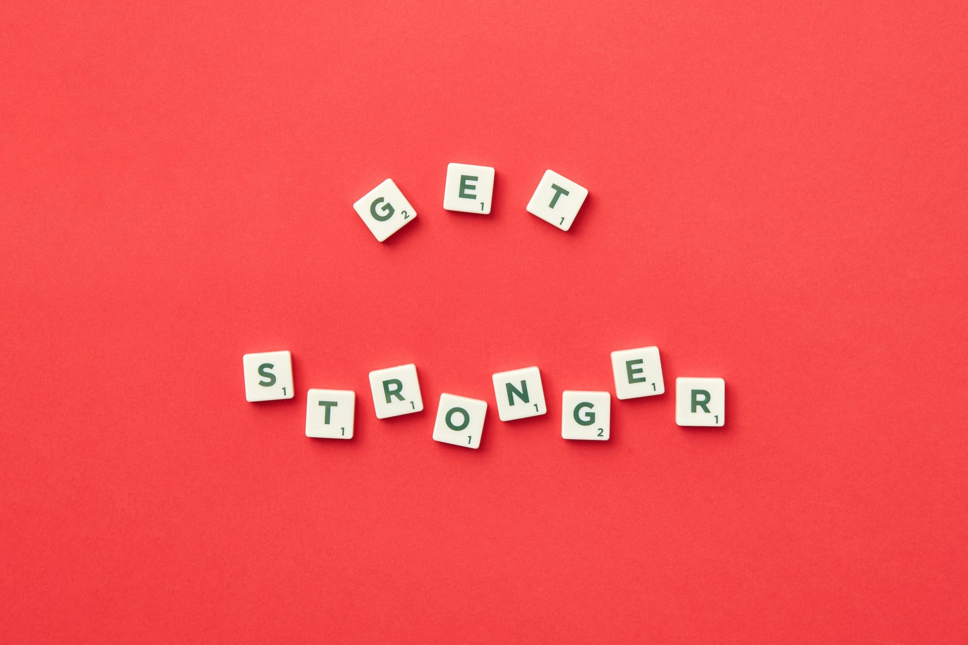 Scrabble tiles on red background spell “GET STRONGER.”