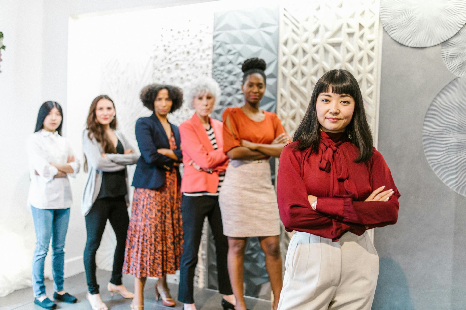 Six people stand in a line against a textured wall, posing with arms crossed in a professional office setting.