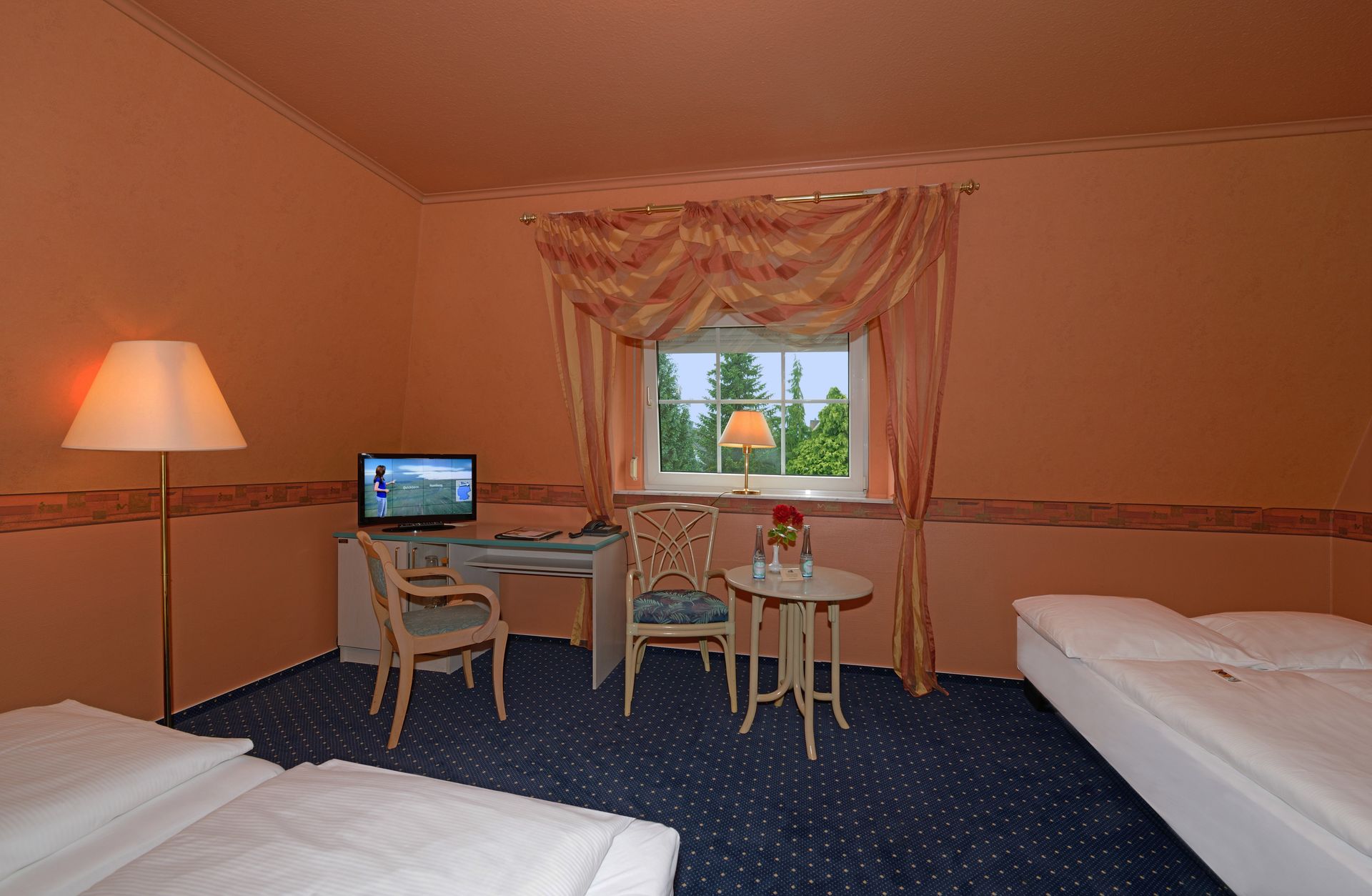 Ein Hotelzimmer mit drei Betten, einem Schreibtisch und einem Fernseher