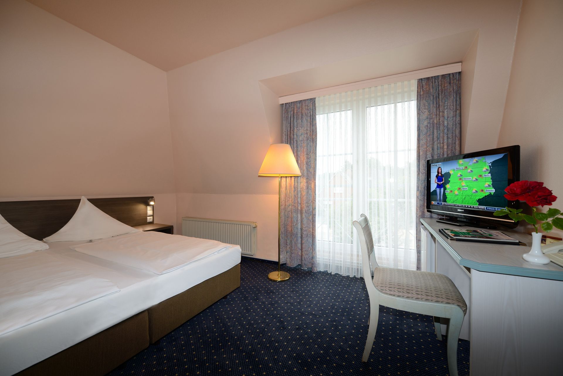 Ein Hotelzimmer mit Bett, Schreibtisch, Stuhl und Fernseher.