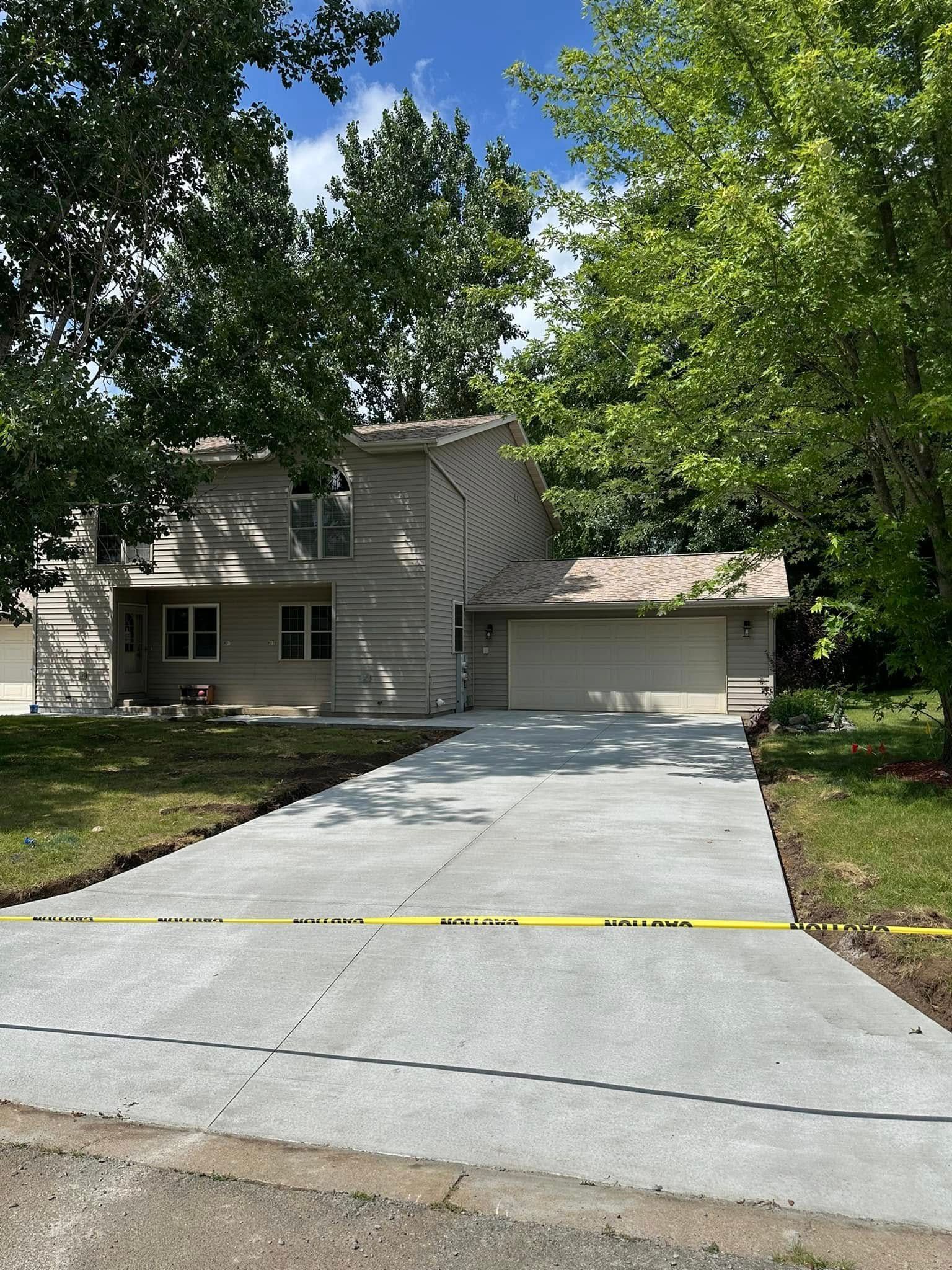 A concrete driveway leading to a house with trees in the background.