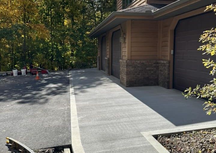 A concrete walkway leading to a garage with trees in the background