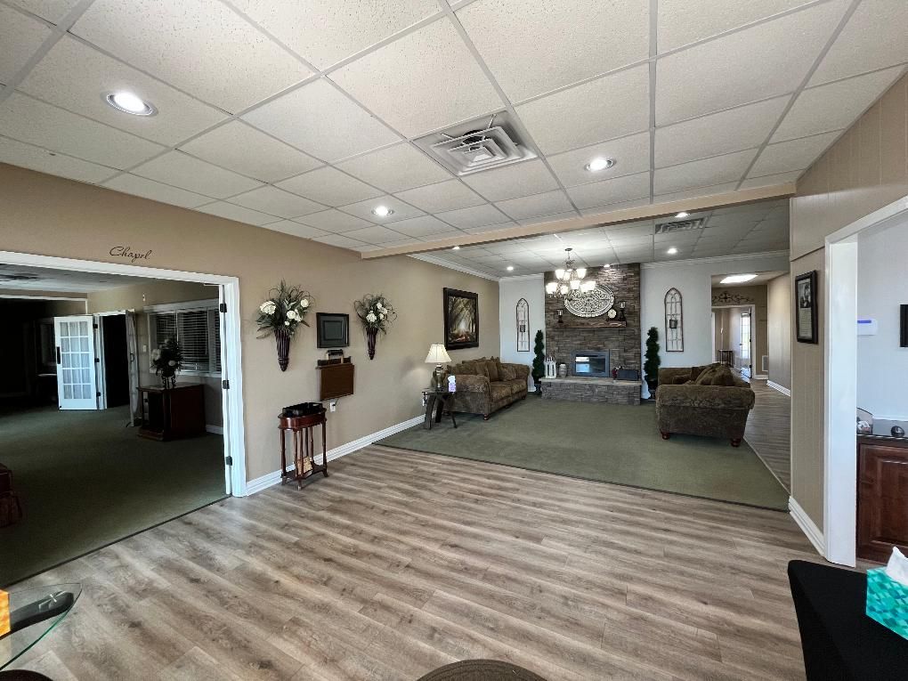Spacious, carpeted room with fireplace, couches, and decorative floral arrangements; likely a waiting or sitting area.