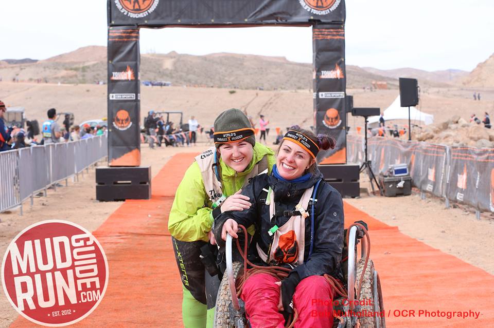 Two women are posing for a picture in front of a sign that says mud run