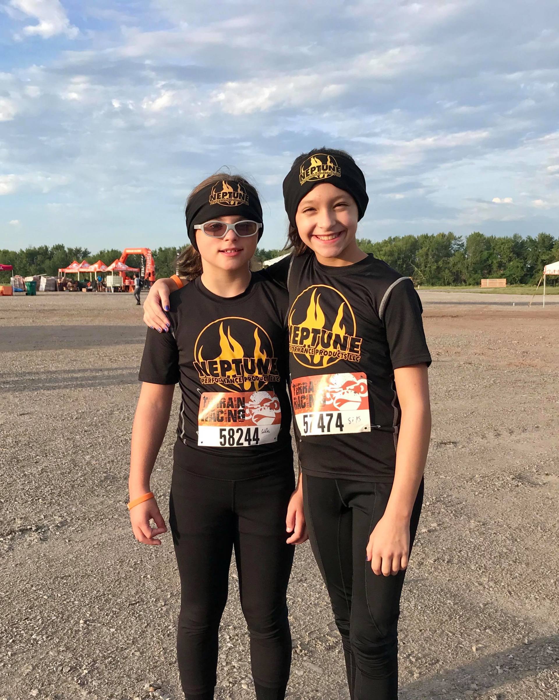 Two young girls are posing for a picture in a parking lot.