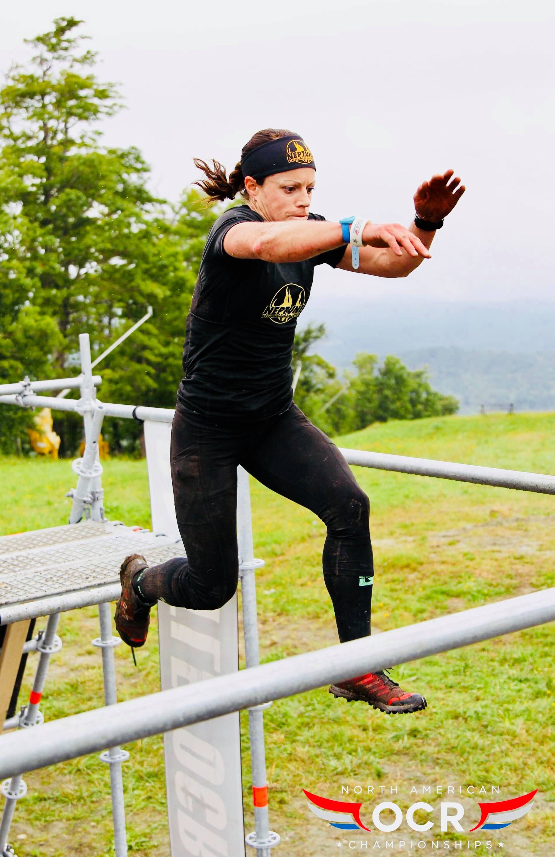 A woman is jumping over a metal bar in a field.