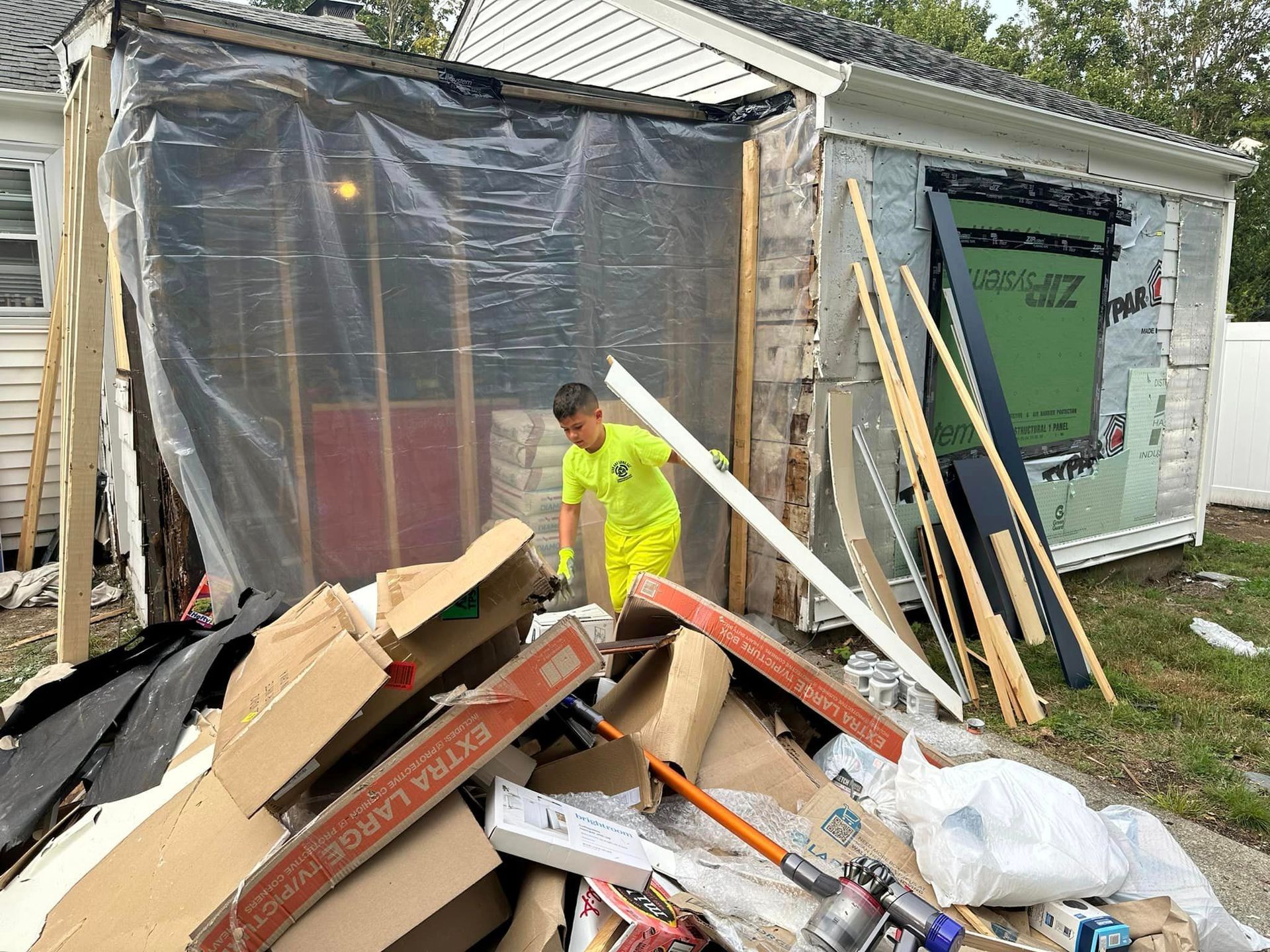 A man in a yellow shirt is standing in front of a pile of cardboard boxes.