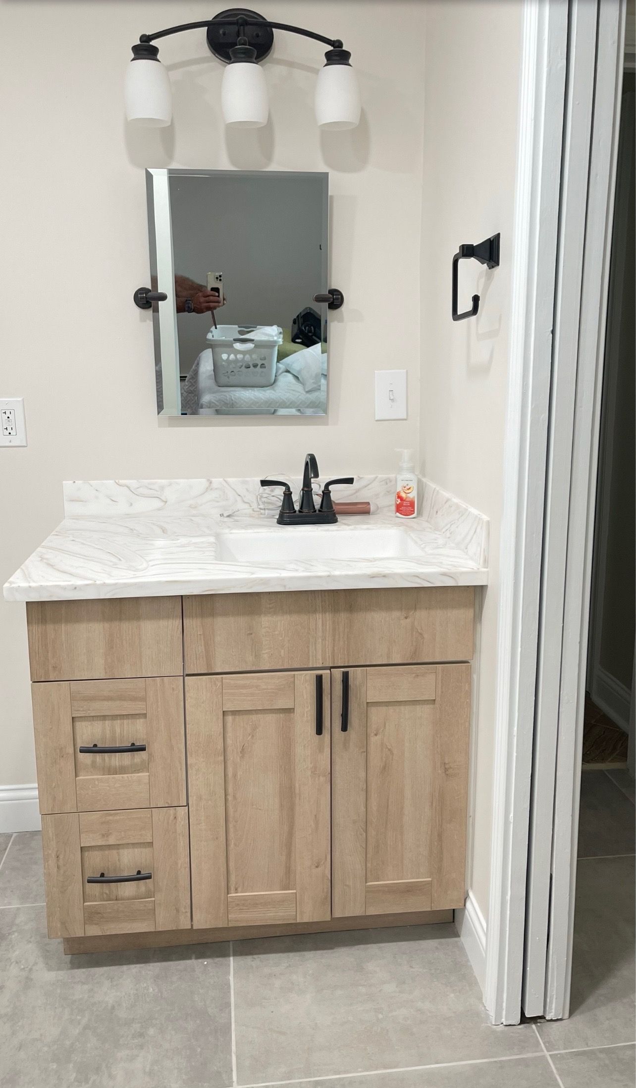 Small bathroom vanity with light wood cabinet, marble countertop, mirror, and wall sconce lighting.