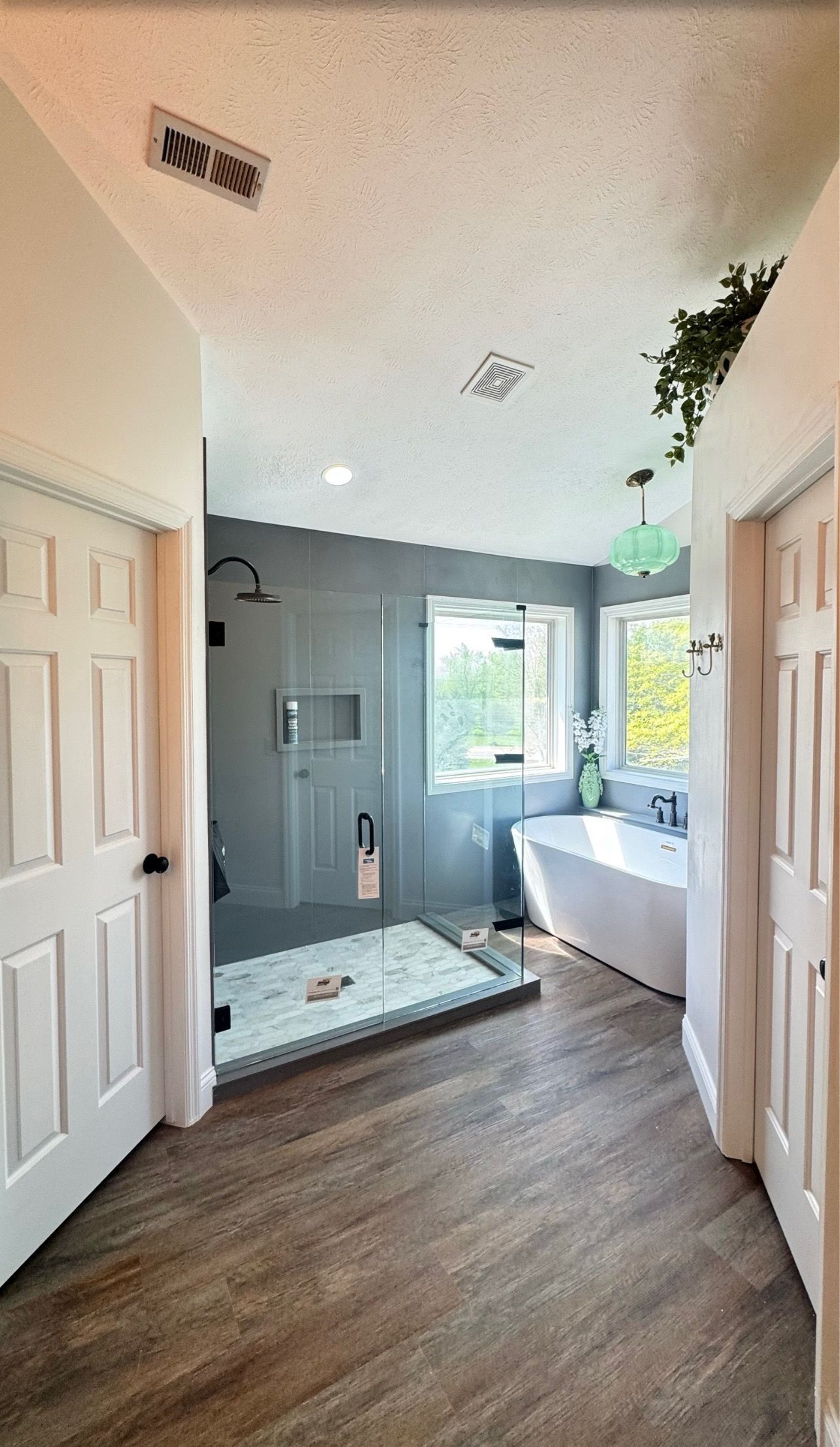 Bright bathroom with gray shower tile, white tub, double doors, wood floor, and a window seat.