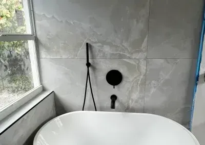 Modern bathroom with a freestanding tub, gray tile wall, and window beside it