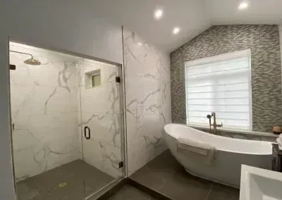 Modern bathroom with glass shower, freestanding tub, marble-look walls, and window blinds