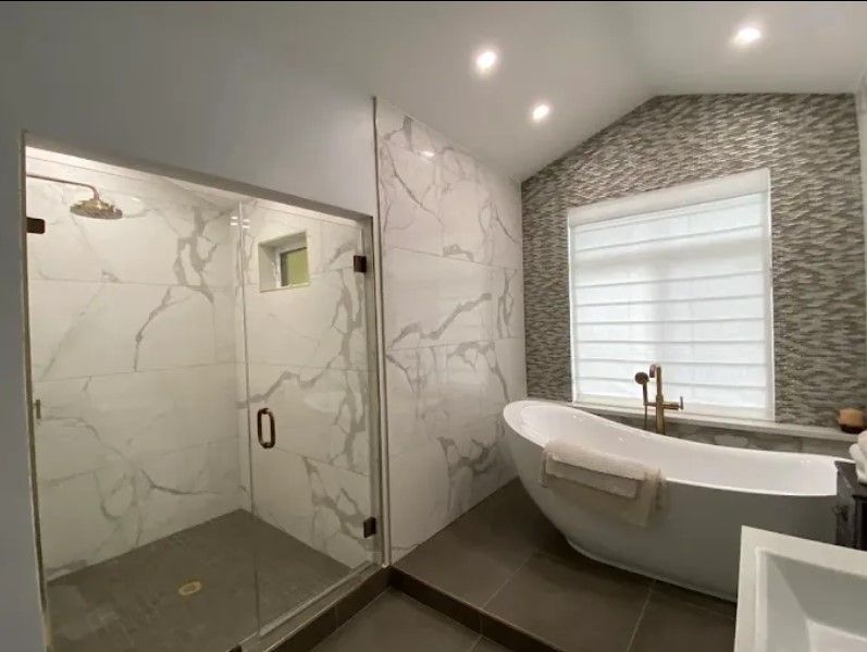 Modern marble bathroom with glass shower, freestanding tub, and window blinds