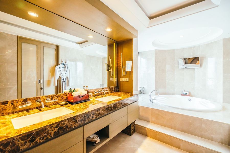Modern luxury bathroom with marble vanity, large mirror, and a white soaking tub by a window.