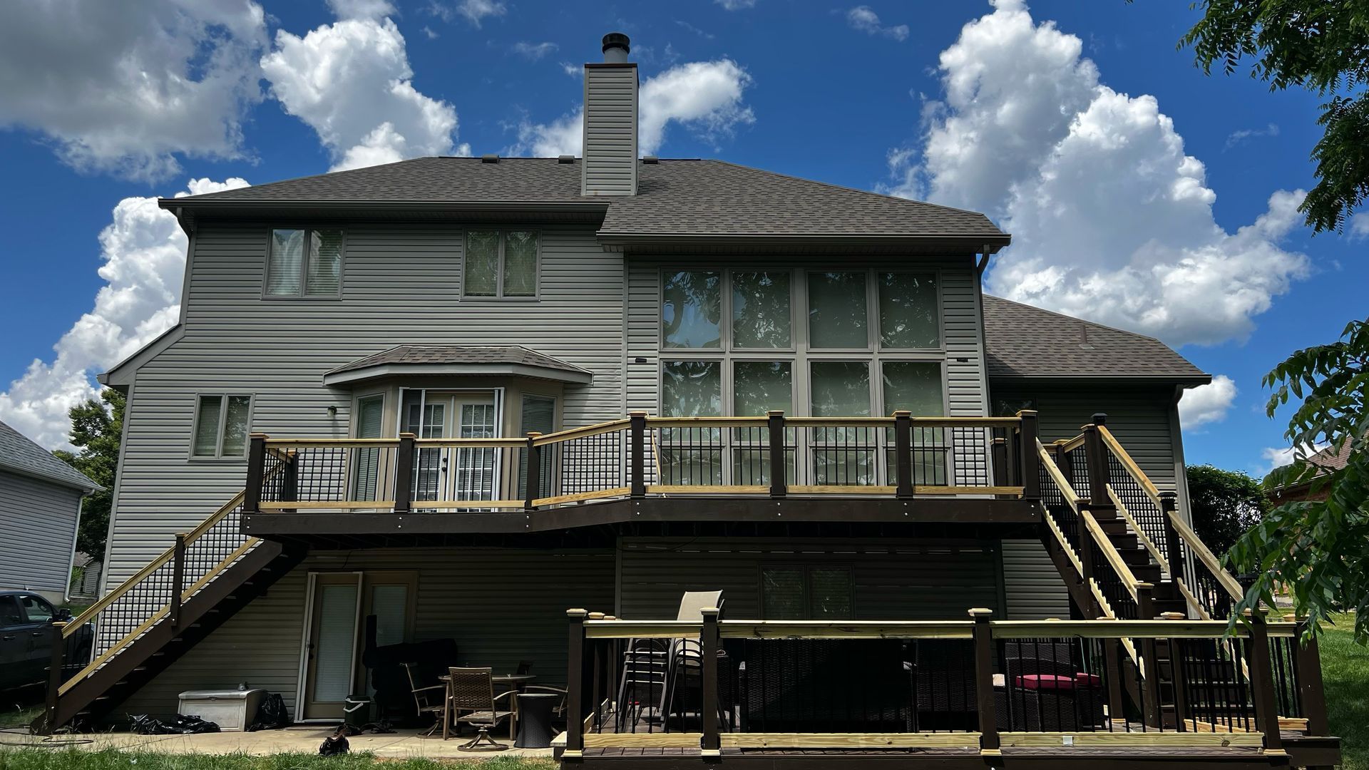 Large two-story gray house with wraparound balcony and outdoor stairs under a blue sky with clouds