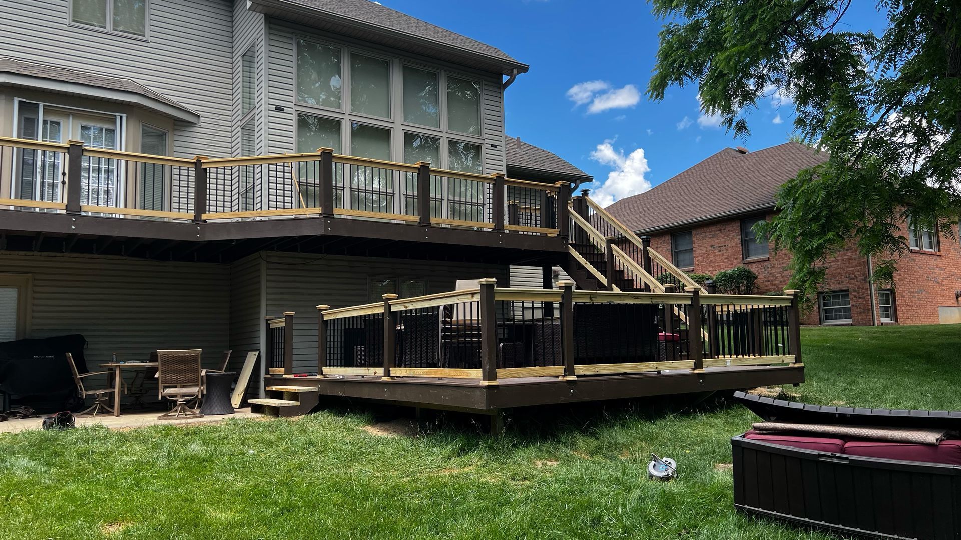 Backyard deck attached to a house with patio furniture and a grassy lawn under a blue sky.