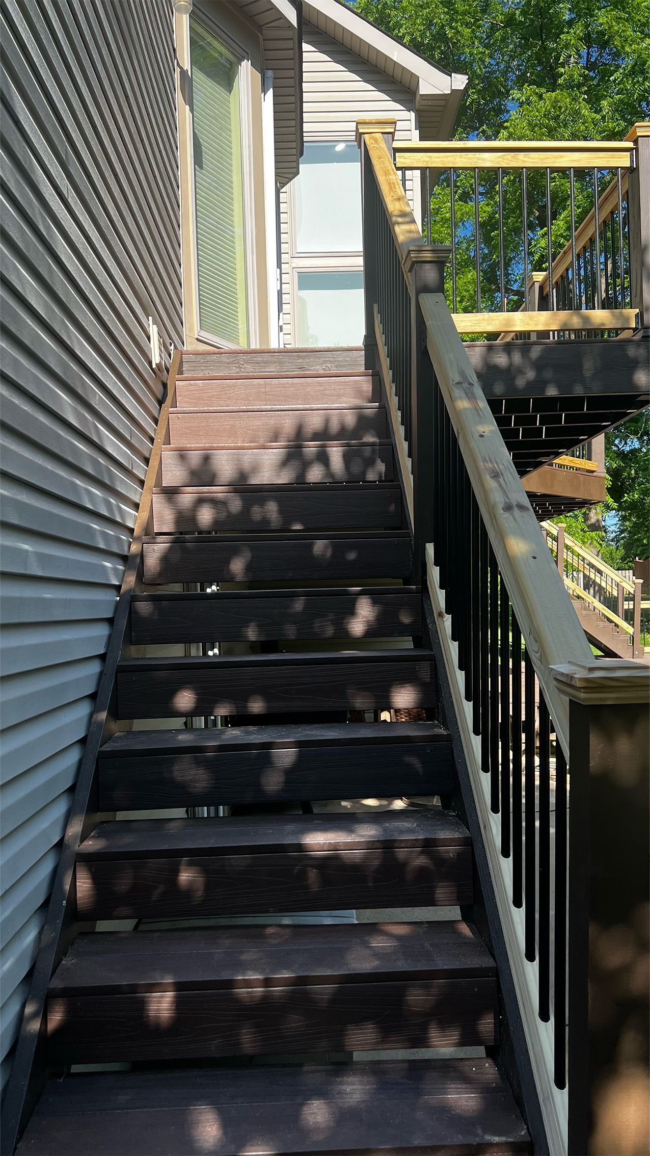 Outdoor wooden staircase beside a house, with railing and dappled sunlight.