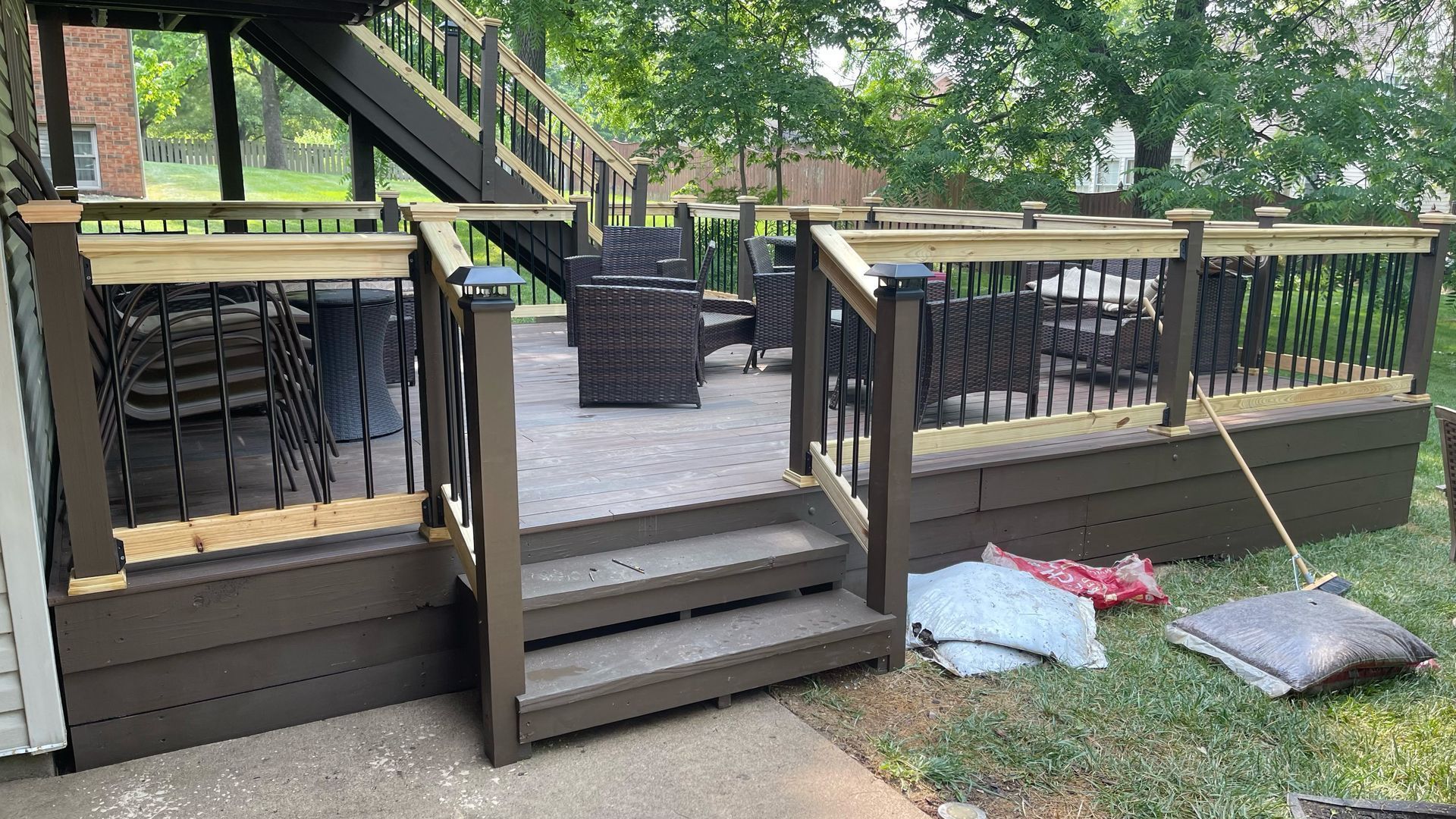 Backyard deck stairs with black railings, chairs under the deck, and cushions on the grass