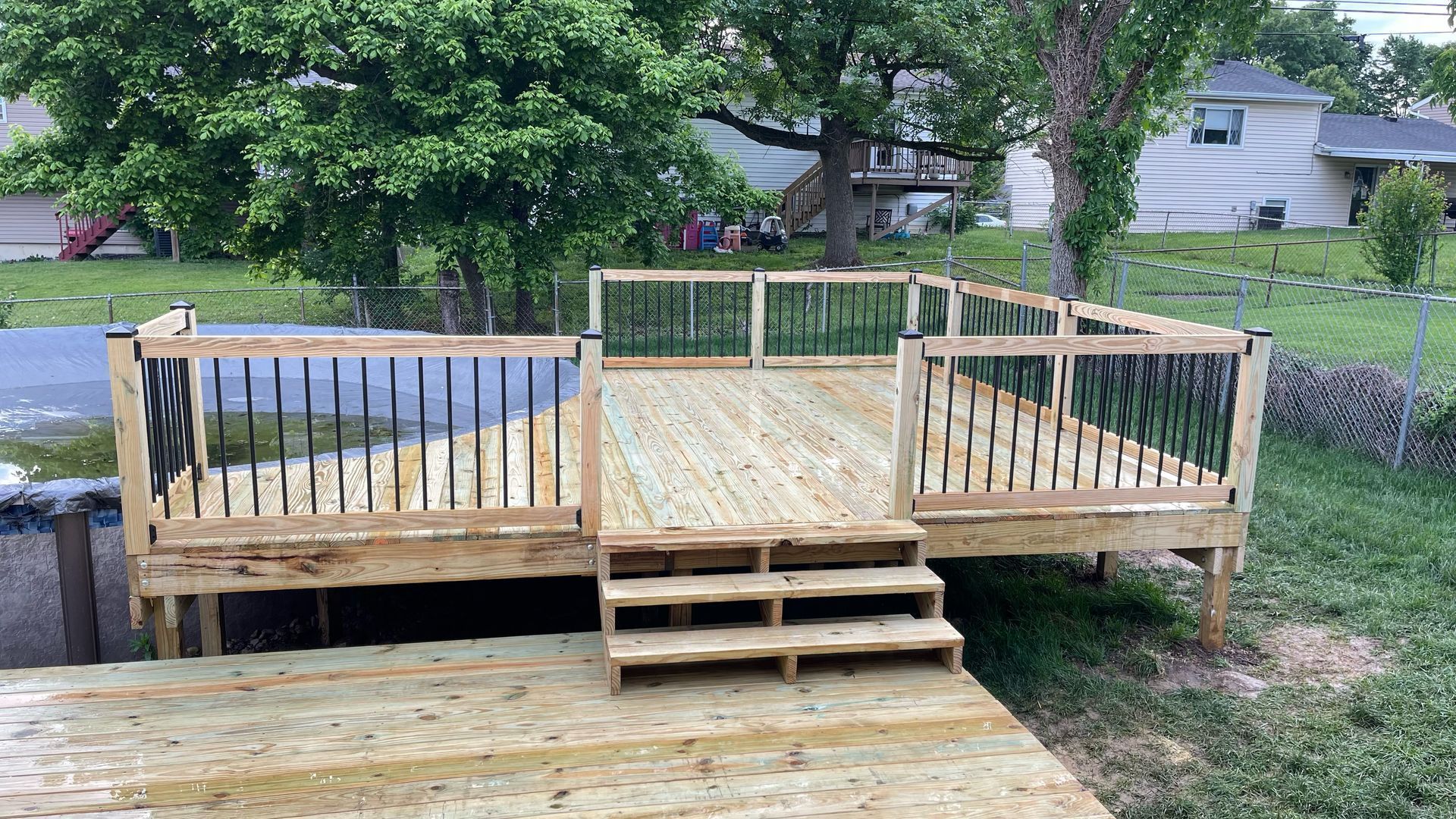Wooden backyard deck with central steps, railings, and a green trellis fence in a grassy residential yard.