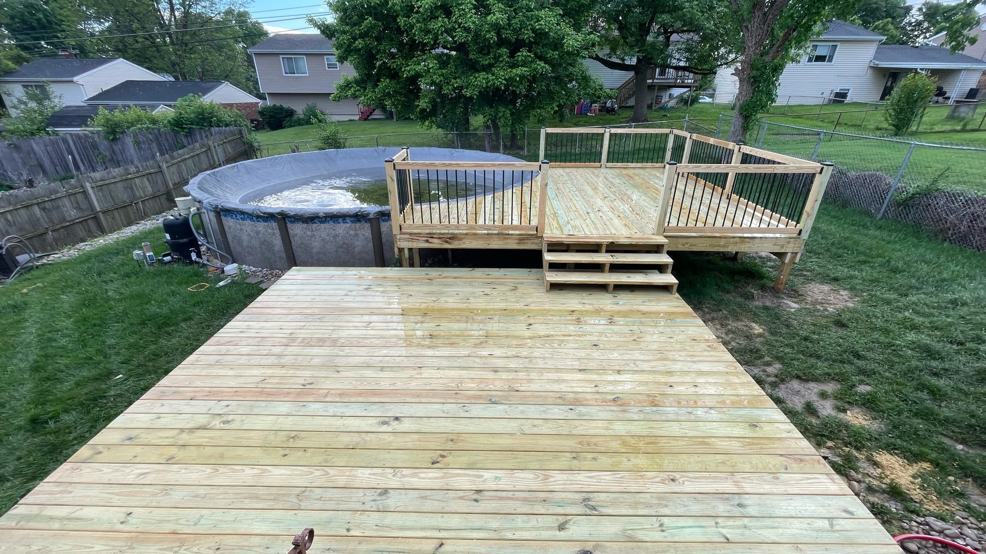 Backyard wooden deck under construction with steps and railing beside an above-ground pool