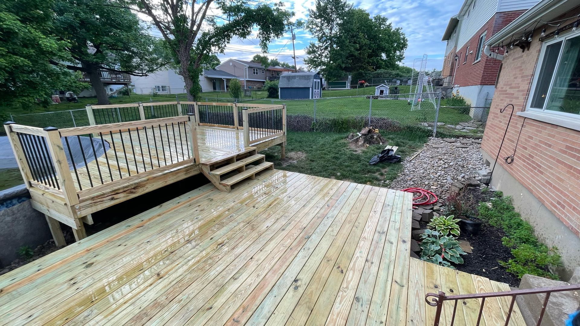 New wooden backyard deck with railings beside a brick house and landscaped yard