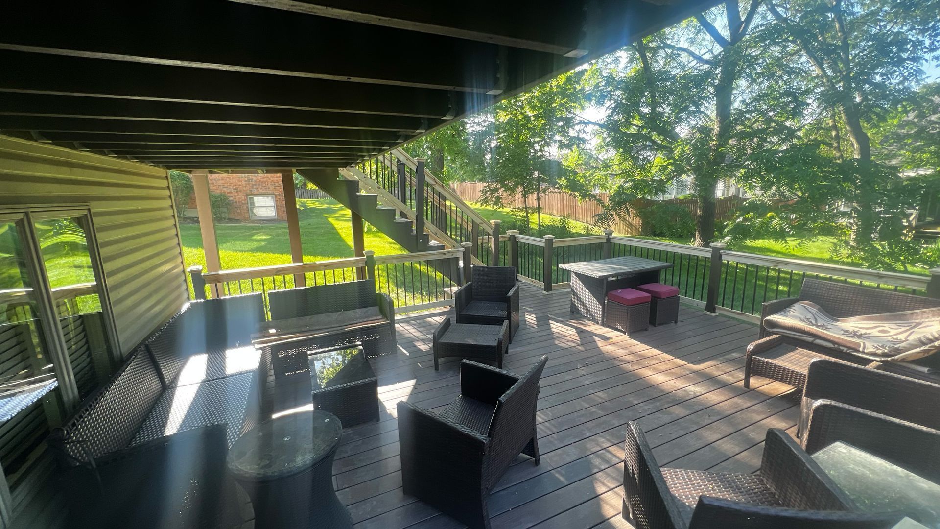 Covered wooden deck with patio furniture and trees in bright sunlight