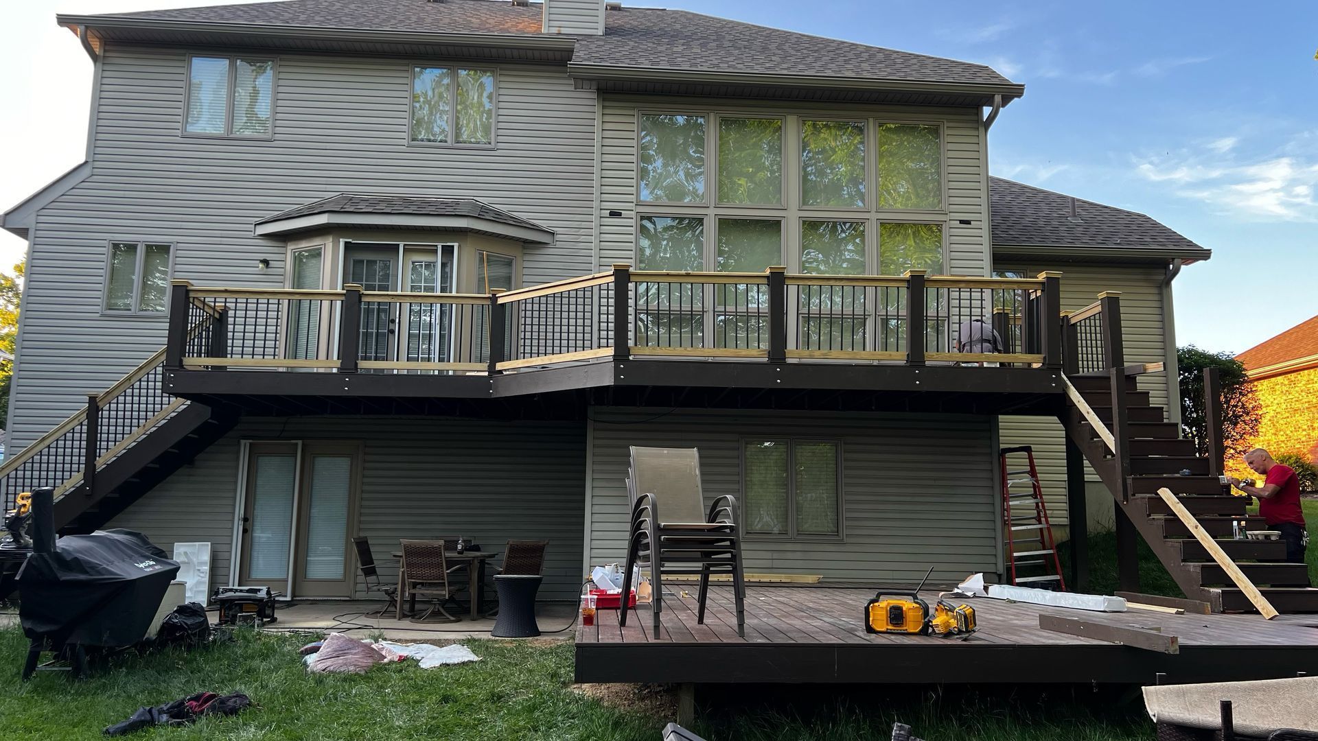Backyard view of a two-story gray house with a raised deck, stairs, and patio furniture at dusk