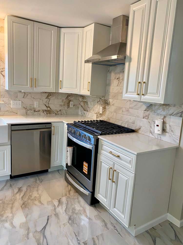 Modern kitchen with white cabinets, marble-look counters and floor, stainless dishwasher, stove, and range hood.