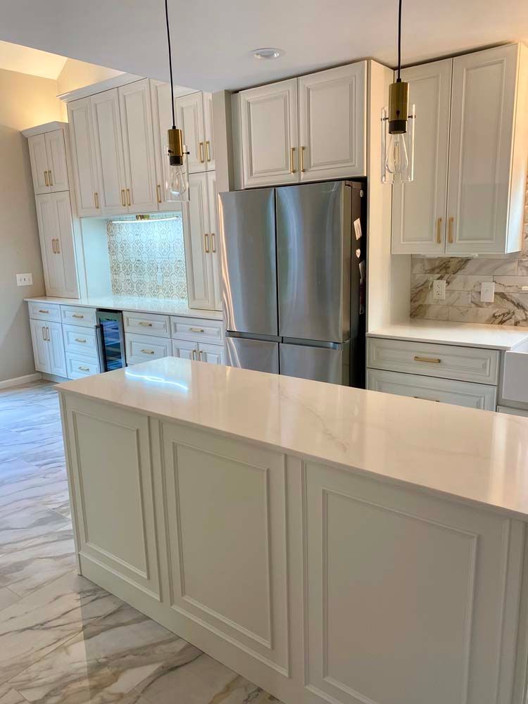 Bright modern kitchen with white cabinets, marble counters, stainless steel fridge, and a large island.
