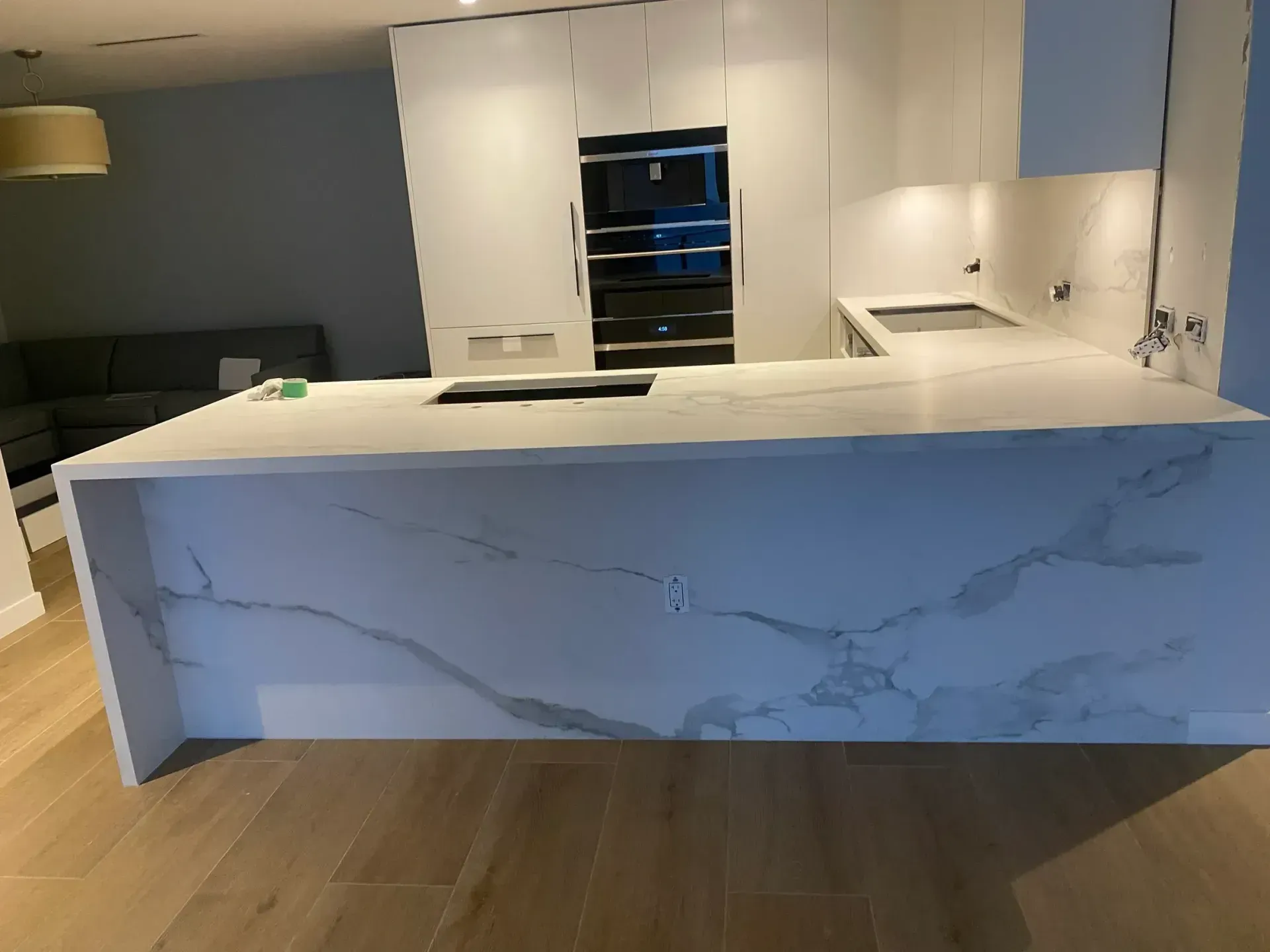 Modern white kitchen with marble island, wood floor, black range hood, and built-in oven