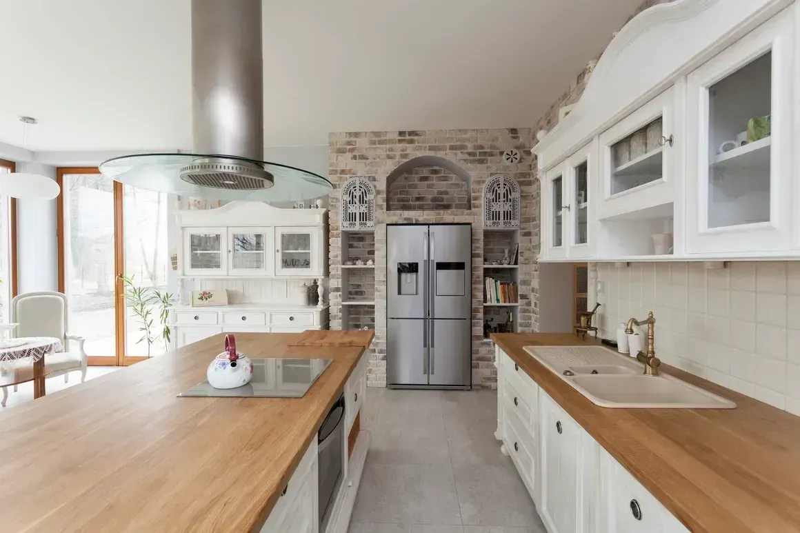 Bright modern kitchen with white cabinets, wooden island, stainless fridge, and stone accent wall