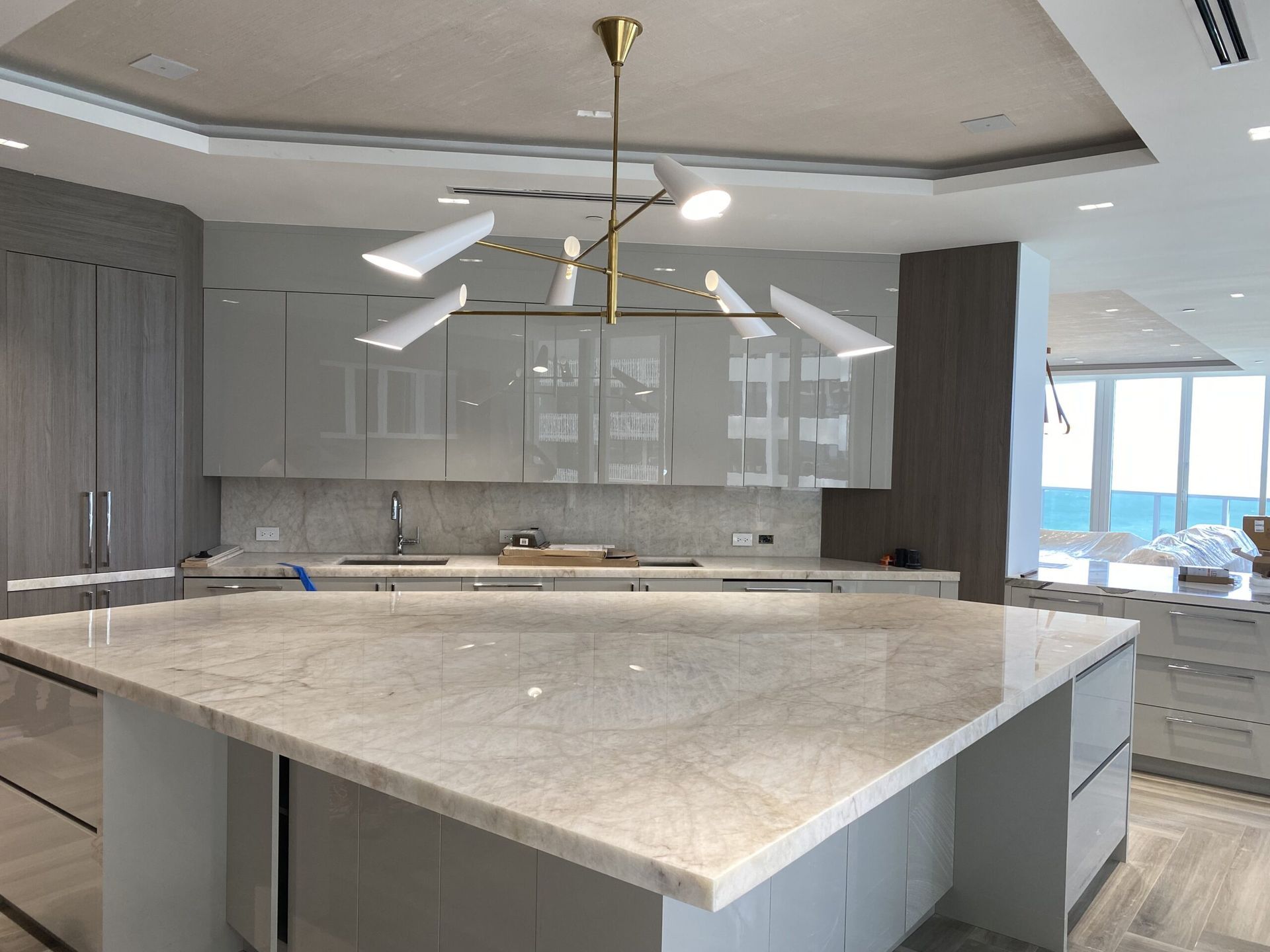 Modern kitchen with a large marble island, gray cabinetry, and pendant lights overlooking water views