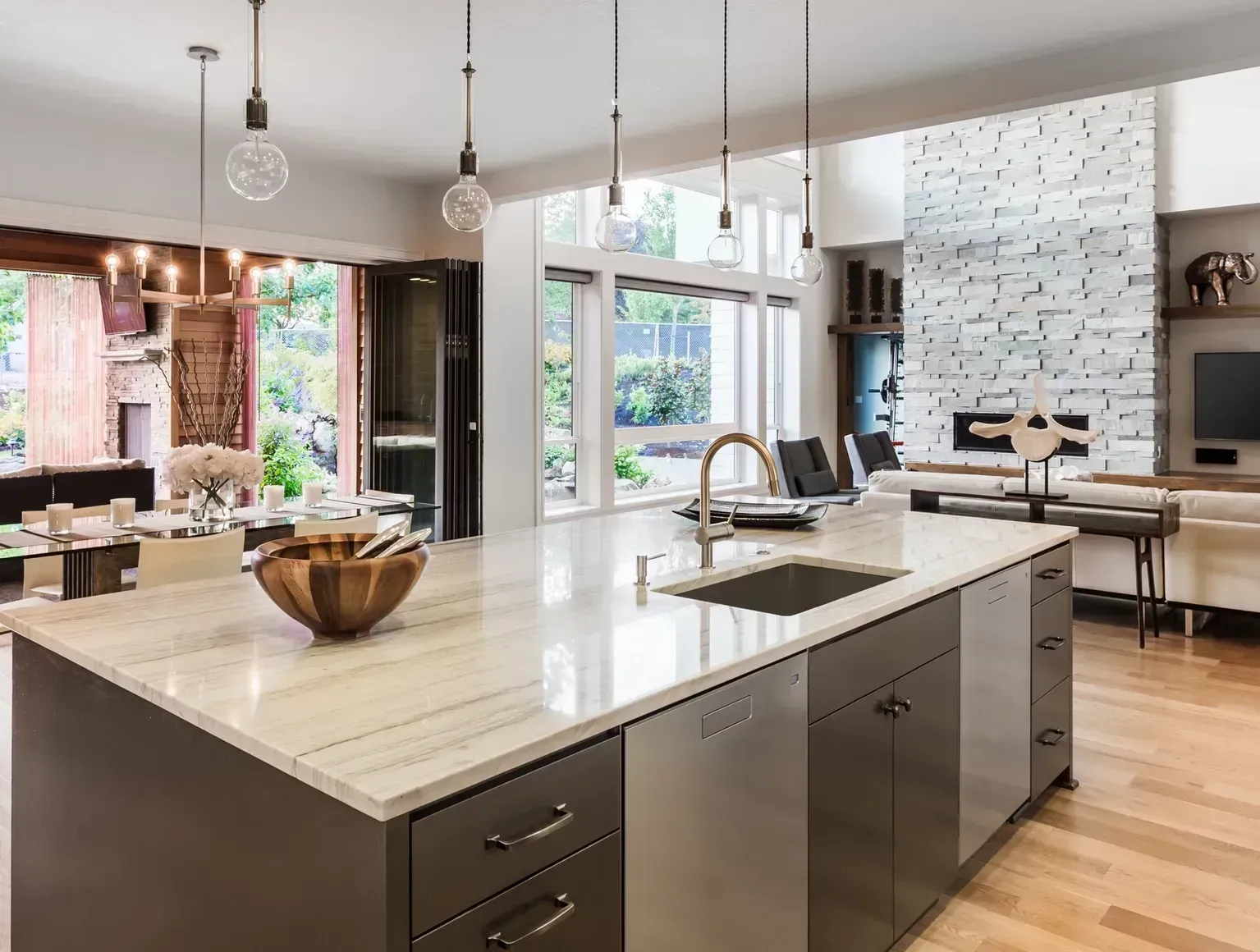 Modern kitchen with large island, white countertops, dark cabinets, and open view to bright living area