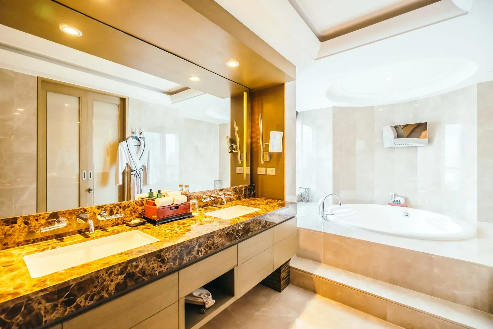 Luxurious bathroom with double vanity, large mirror, and white soaking tub under warm lighting