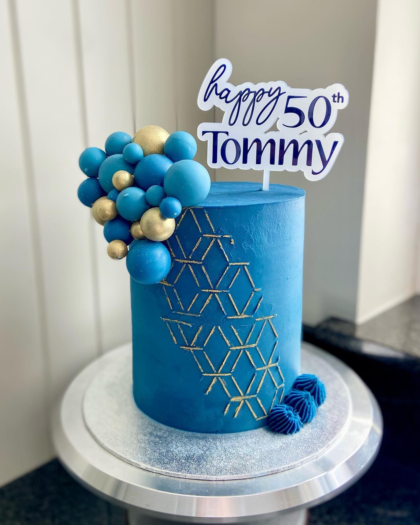 A blue and gold birthday cake with a happy 50th tommy cake topper.