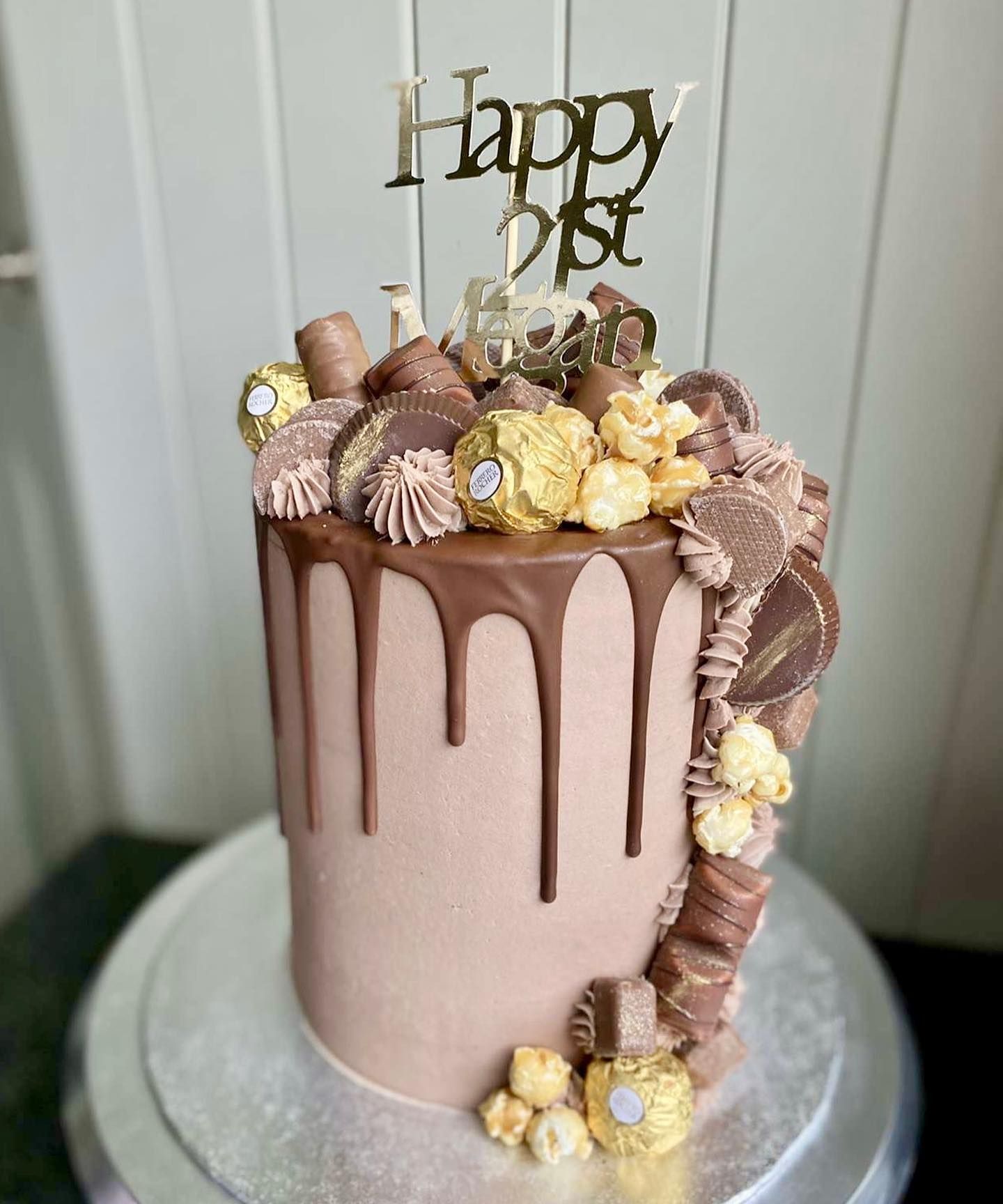 A chocolate drip cake with a happy 1st birthday topper is sitting on top of a cake stand.