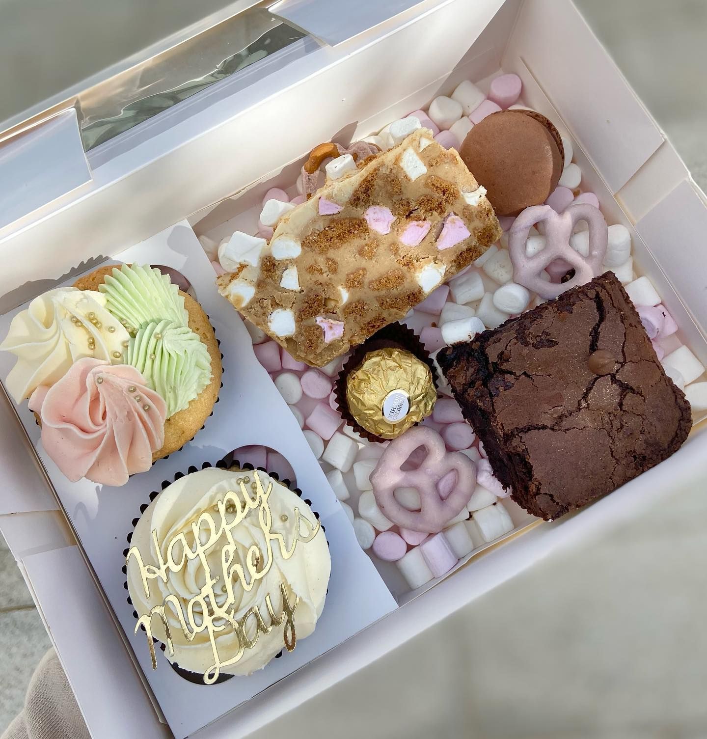 A box filled with cupcakes , brownies , pretzels and marshmallows.