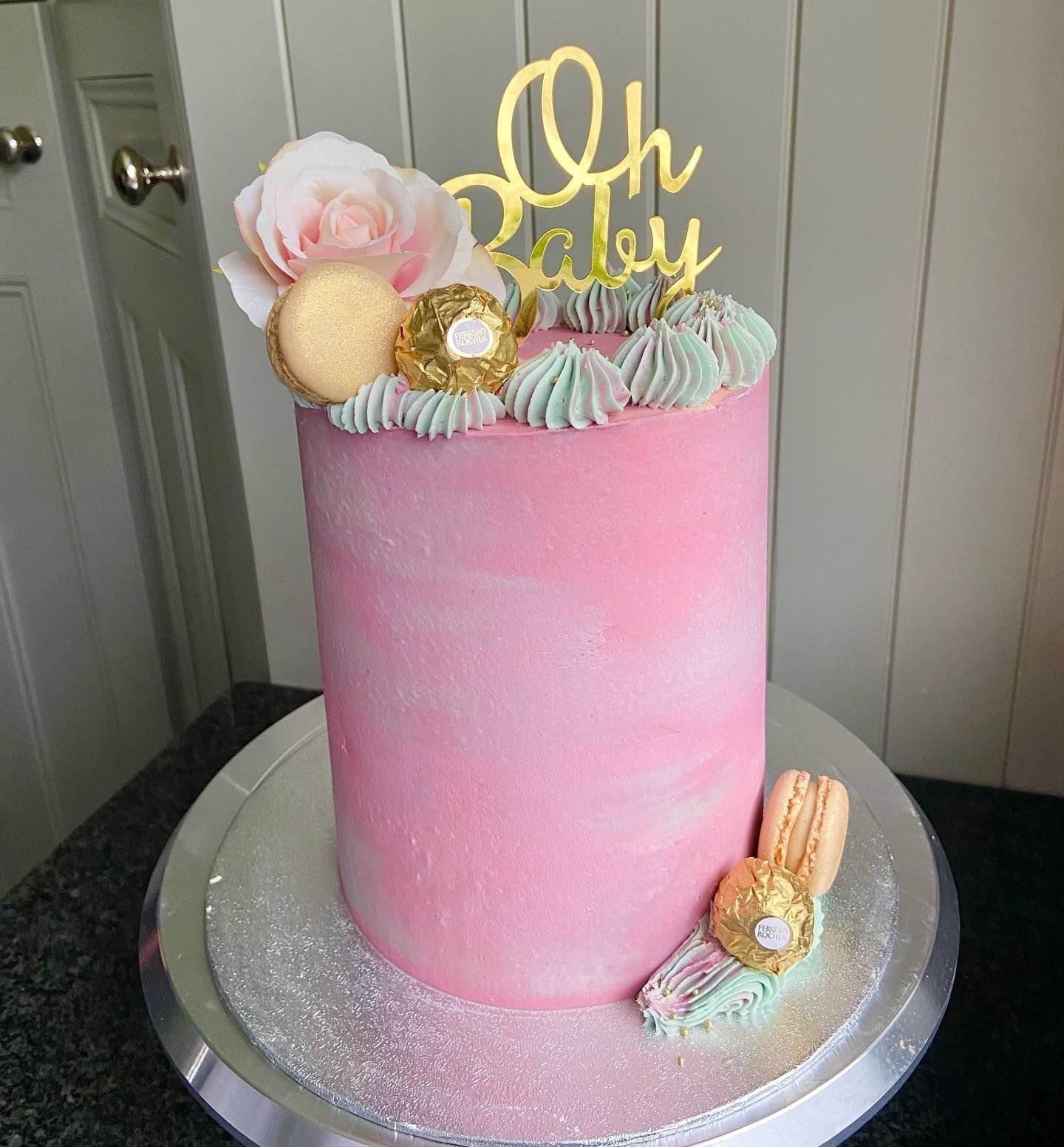 A pink cake with a topper that says oh baby