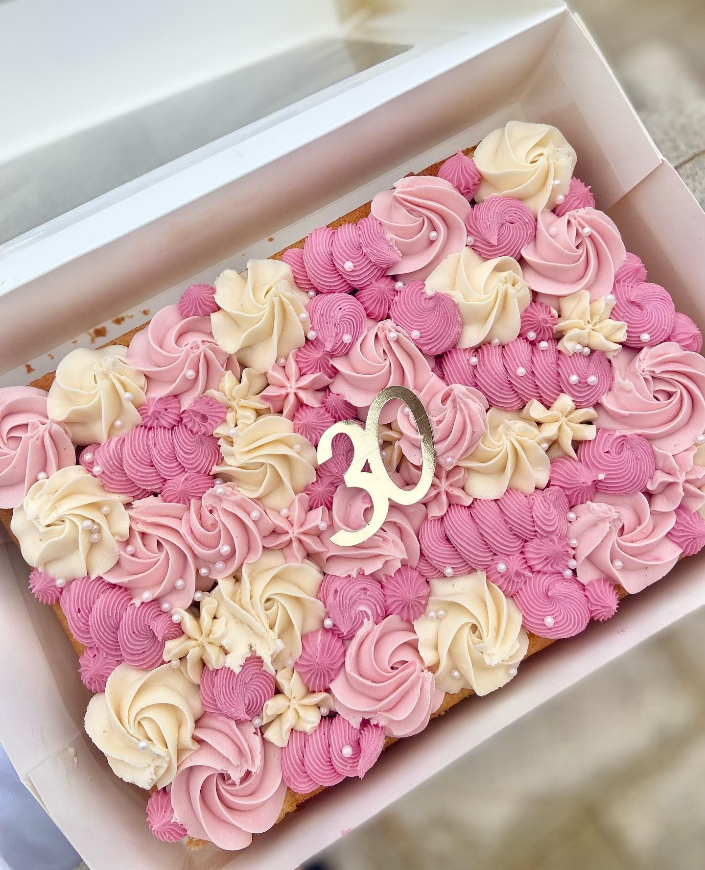 A cake with pink frosting and the number 30 on it is in a box.