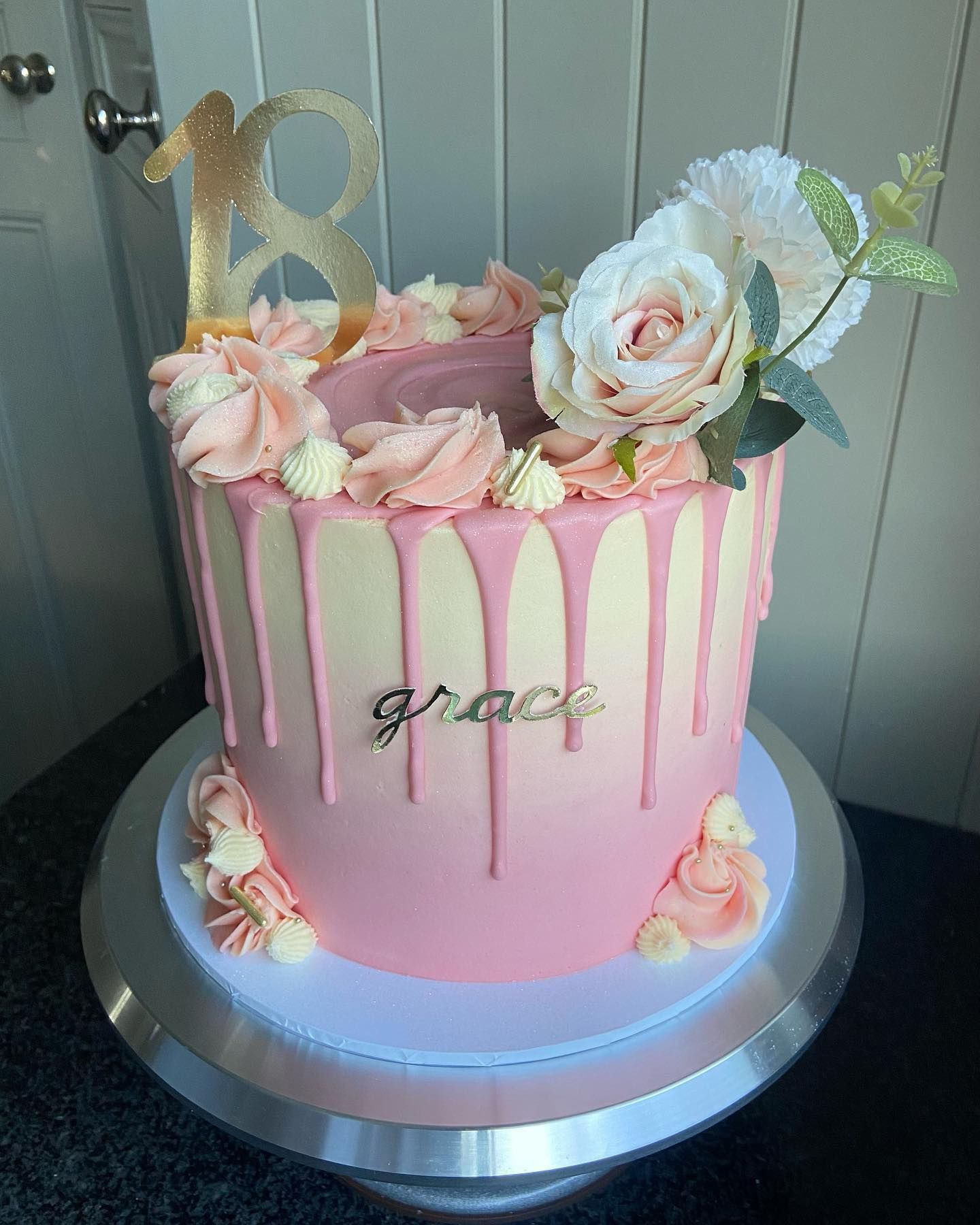A pink and white cake with flowers on top is on a silver plate.