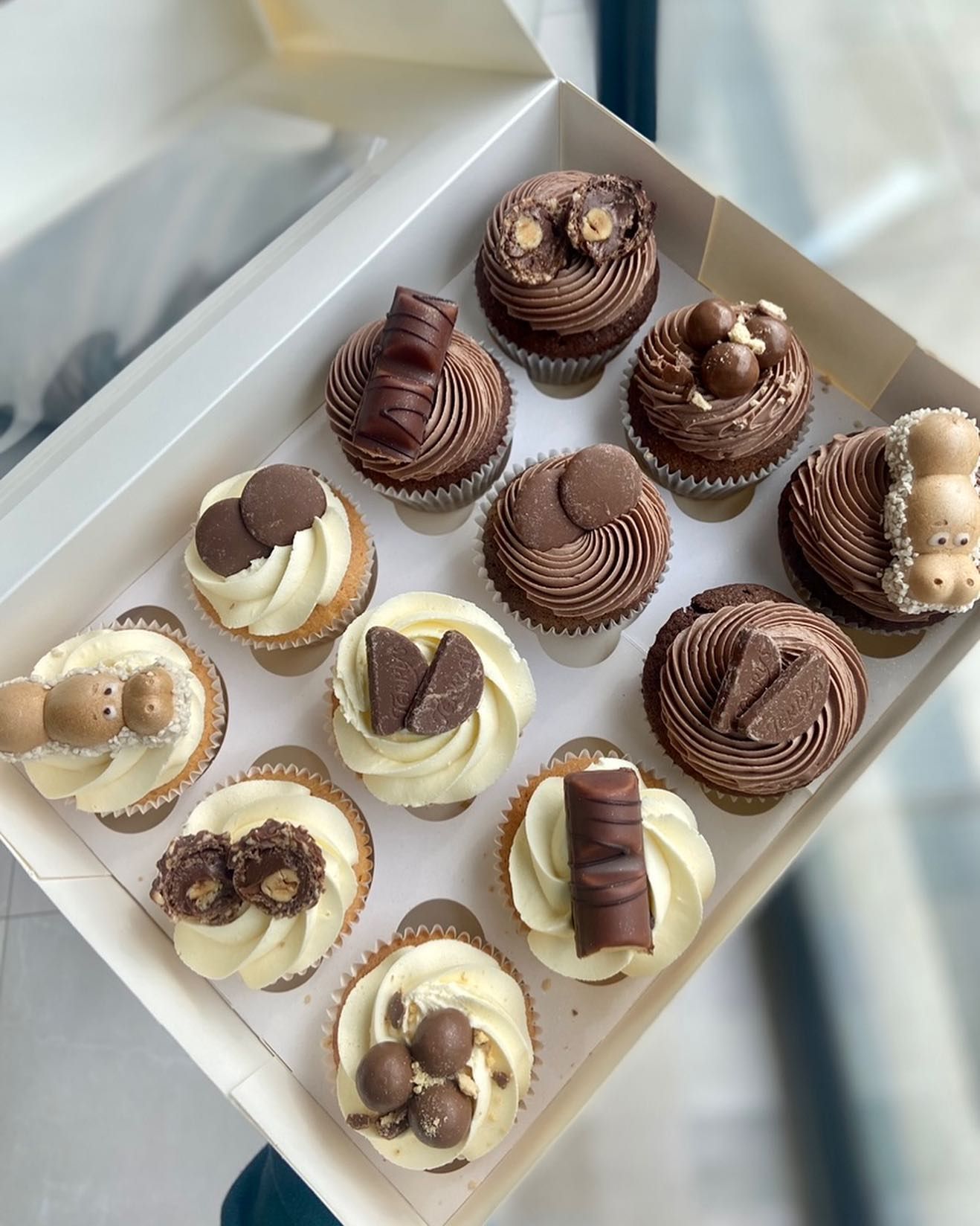 A box of cupcakes with chocolate frosting and decorations