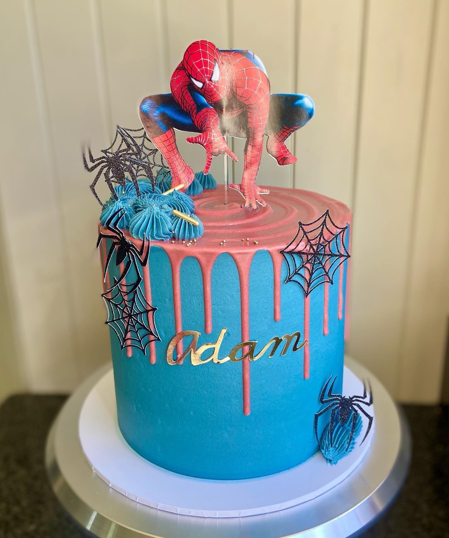 A blue and pink cake with a spiderman on top of it.
