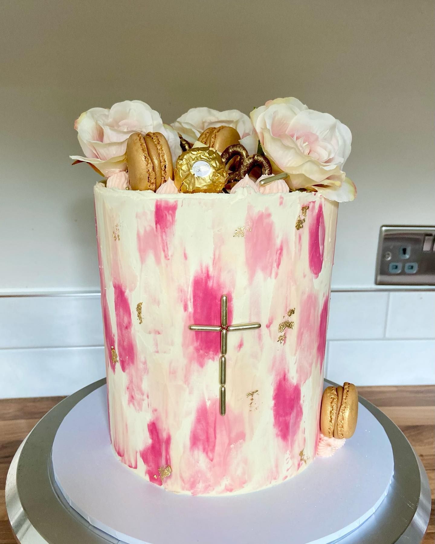 A pink and white cake with a cross on top of it.