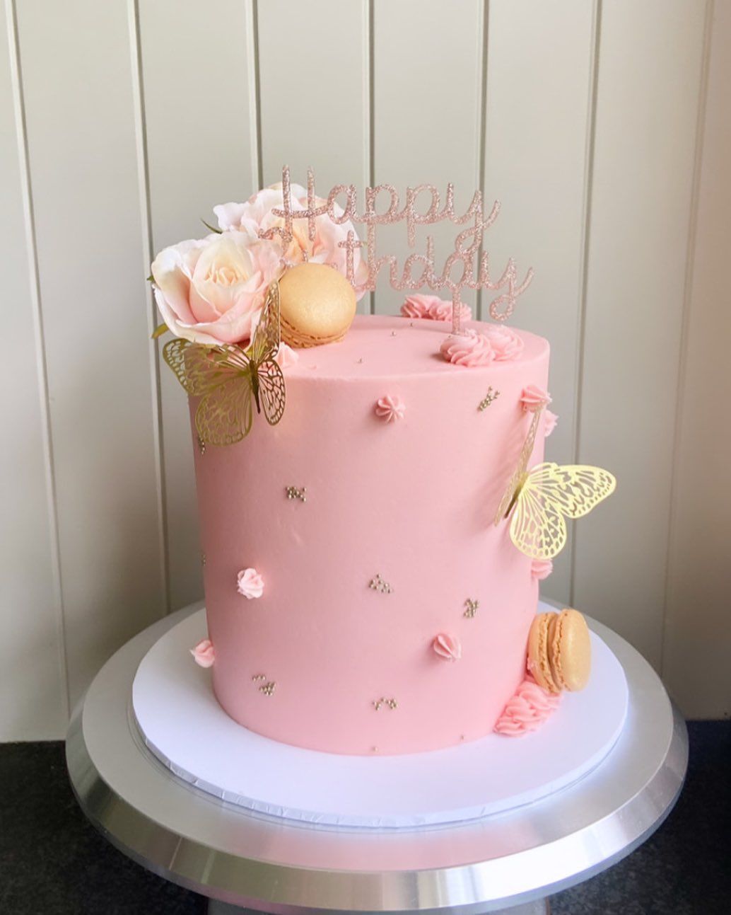A pink cake with flowers and butterflies on it is on a cake stand.