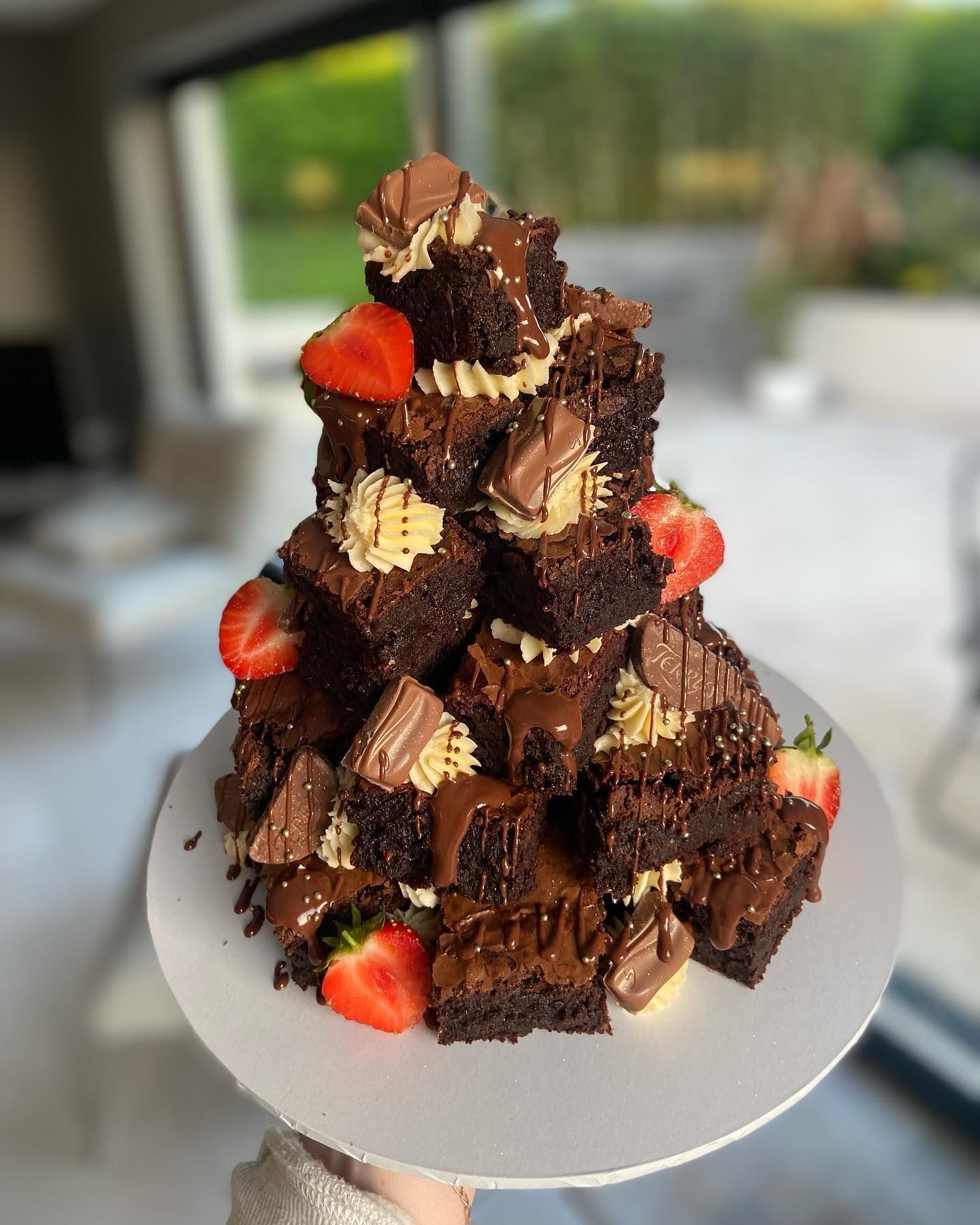 A person is holding a plate of brownies and strawberries.