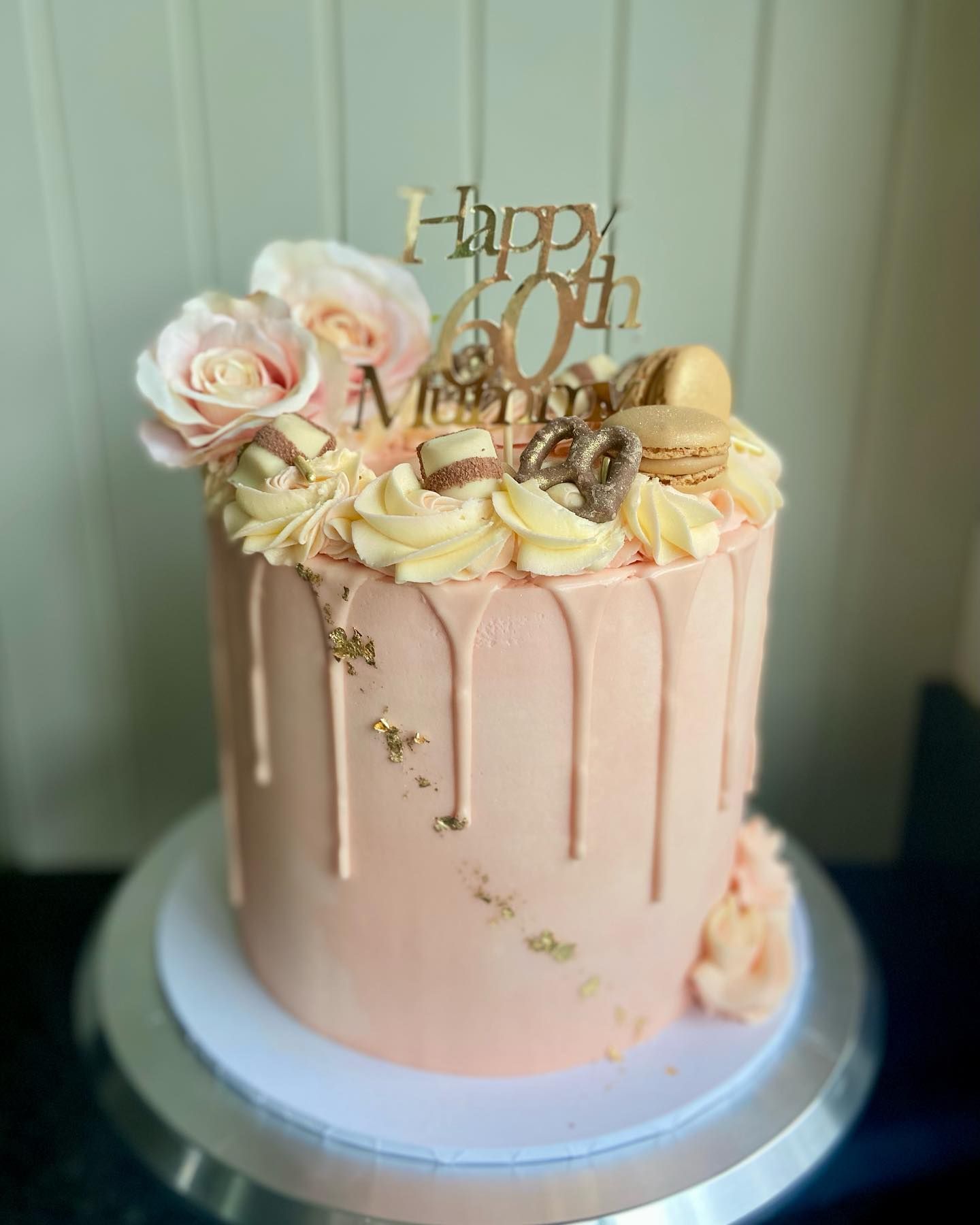 A pink cake with a drip and flowers on top is on a cake stand.