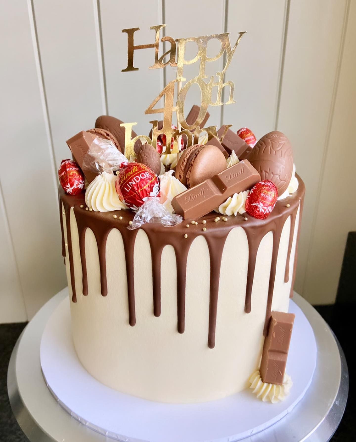 A cake with chocolate drip and a happy 40th birthday topper on top of it.