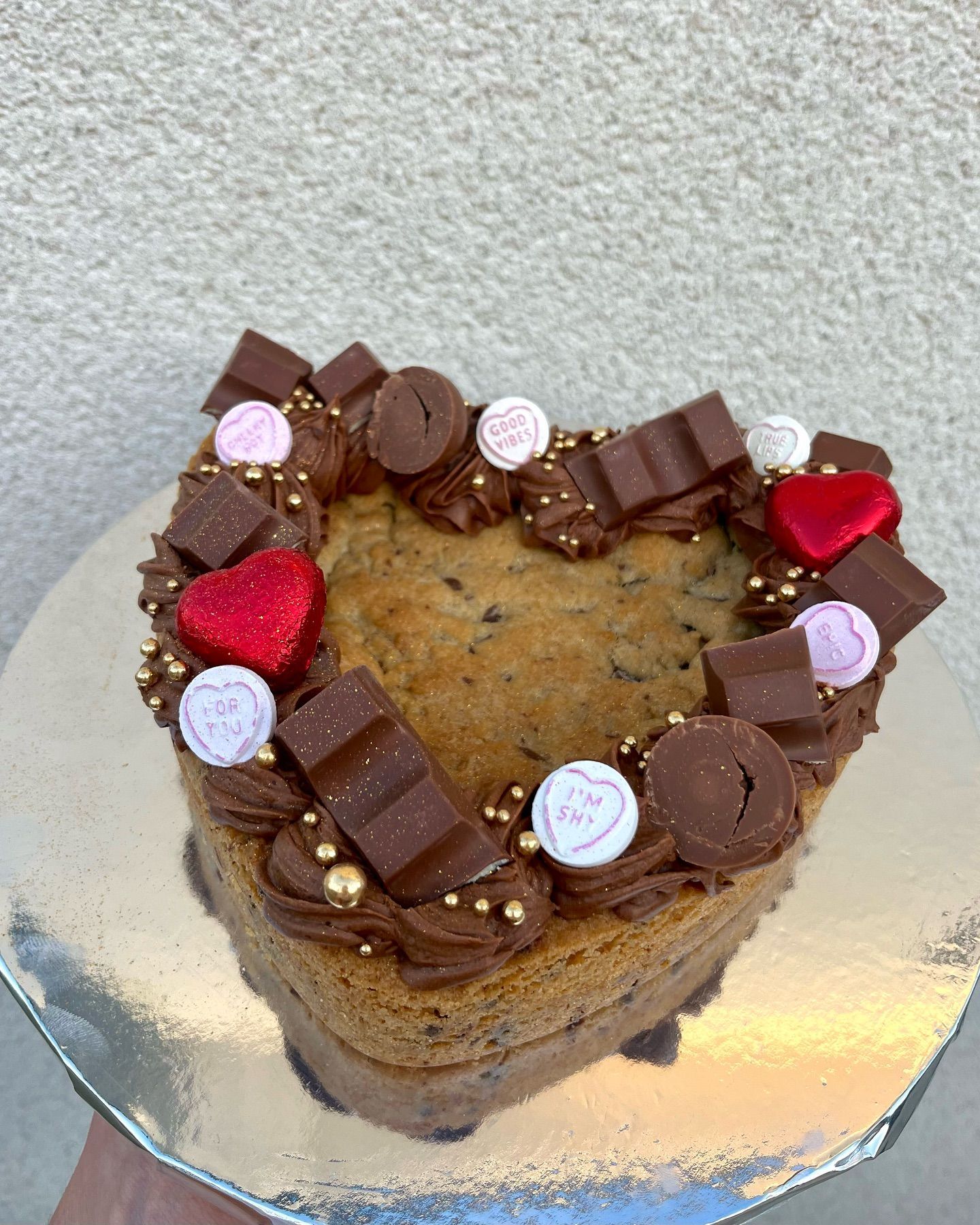 A heart shaped cookie cake with chocolate frosting and candy on top.
