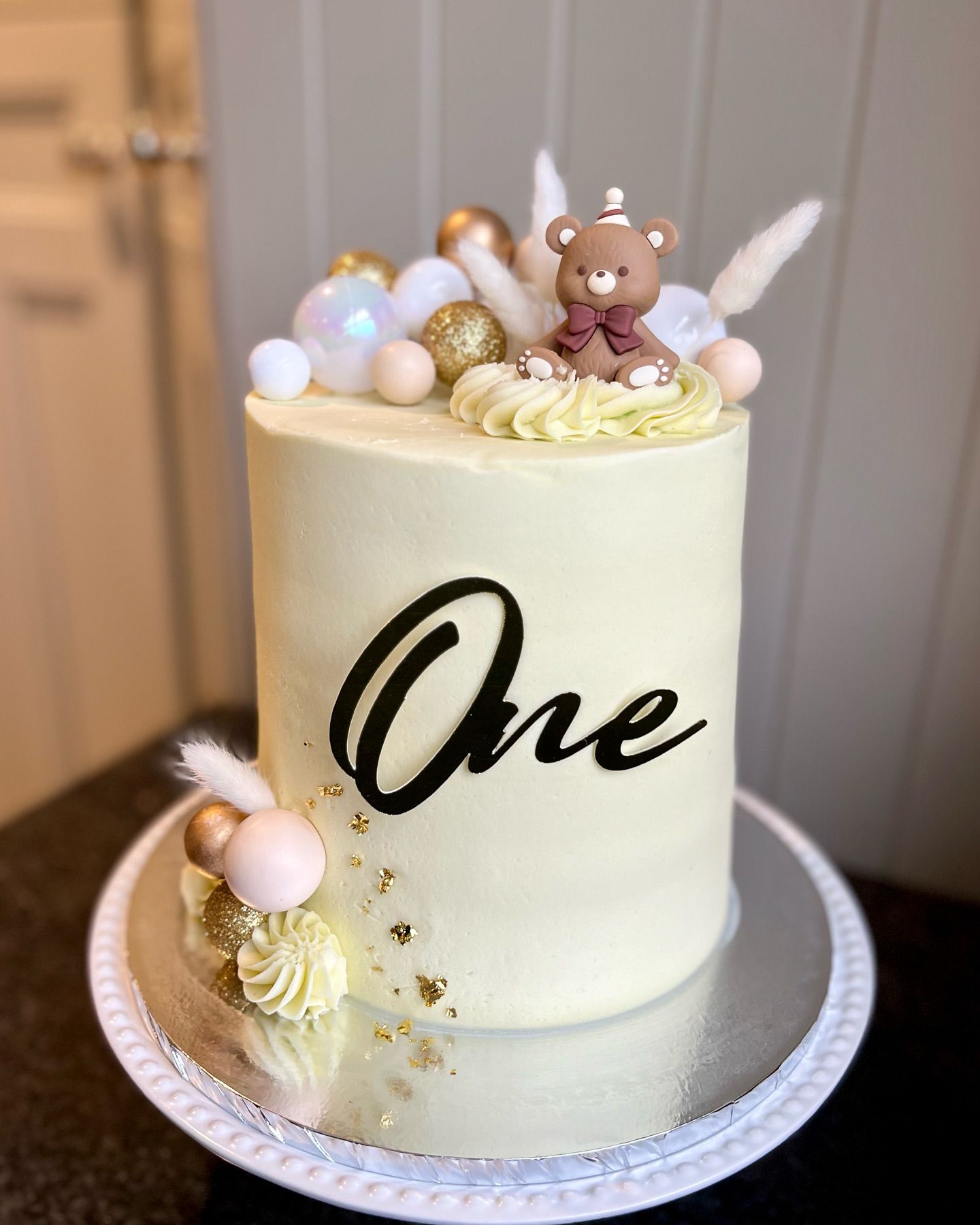 A cake with the word one on it and a teddy bear on top.