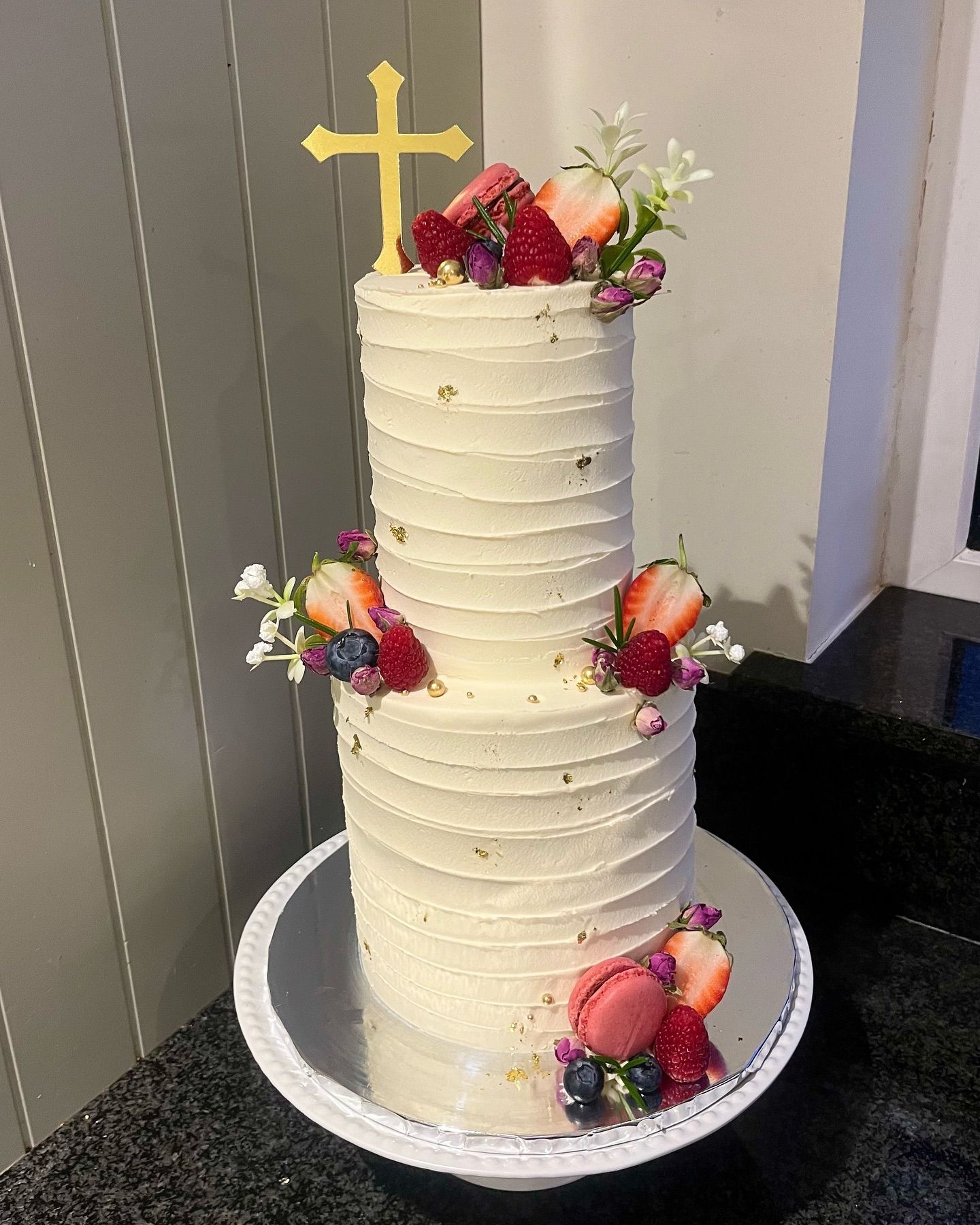 A white cake with flowers and a cross on top is on a plate on a table.