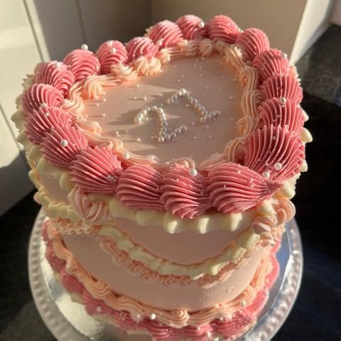 A heart shaped cake with pink frosting and pearls on a plate.
